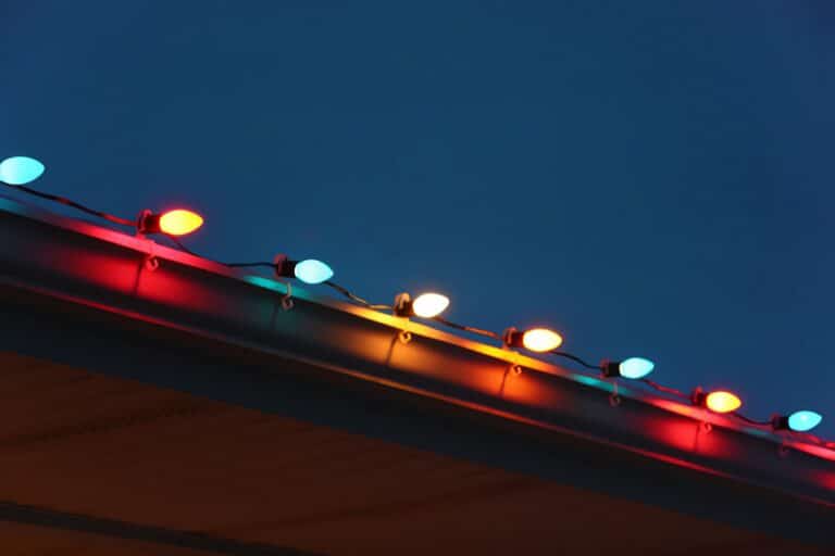 A cheerful and colorful holiday background with a closeup of a house roof decorated with detailed and glowing Christmas lights at dusk.